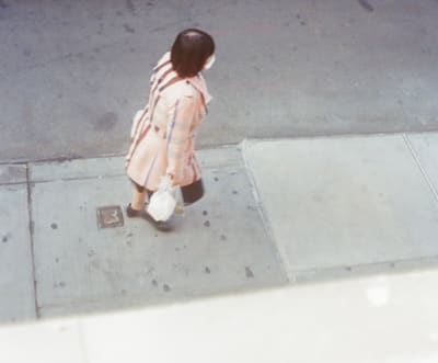 Person in a pale pink checked coat carrying a plastic bag along the curb, seen from above