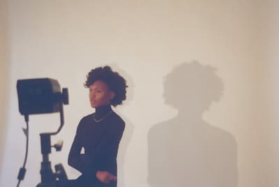 Person in a black turtleneck beside a studio light, their soft shadow on a cream wall