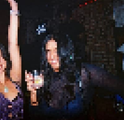 Pixelated photo of a smiling person with long dark hair holding up a drink in a dark club