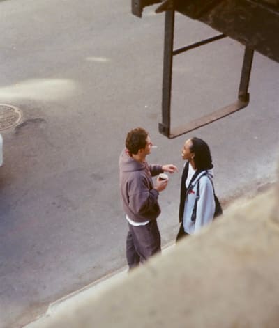 Two people talking on the sidewalk beneath a hanging metal ladder, seen from above