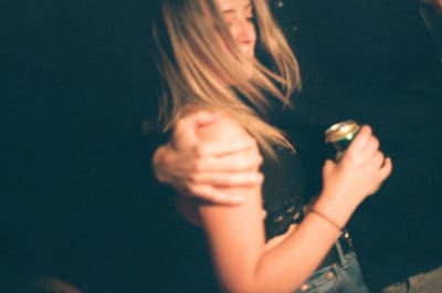 Motion-blurred person with long blonde hair holding a drink can, a hand gripping their shoulder