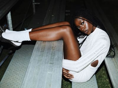 Full-spread flash photo of a model in a white knit dress lying on metal bleachers at night