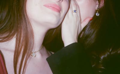 Close-up of two people cheek to cheek, a hand with a blue-stone ring on one face