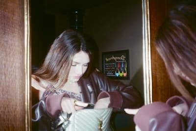 Person looking down into a quilted handbag, seen in a wood-framed mirror