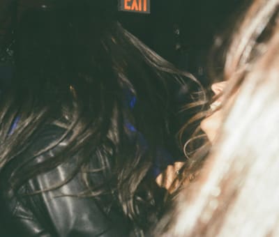 Long dark hair and a black leather jacket in motion under a red EXIT sign
