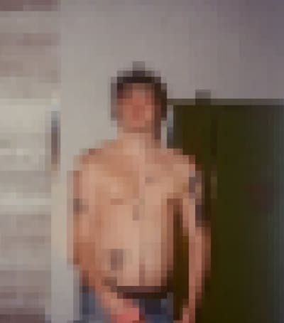 Pixelated photo of a shirtless person standing against a pale wall