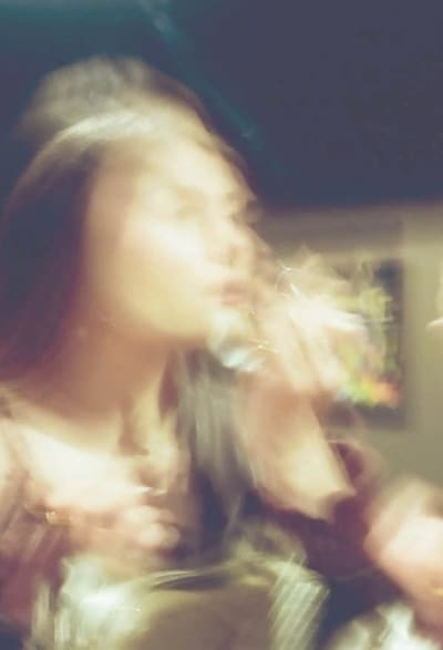Motion-blurred warm photo of a person drinking from a glass in a dim room