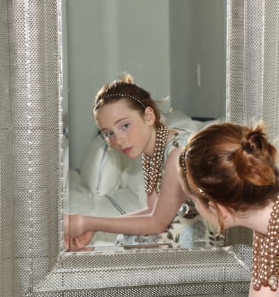 Young model leaning towards an ornate silver mirror, the reflection looking back at the camera