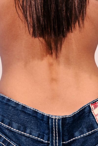 Bare back of a person above low-slung dark-wash jeans with contrast stitching